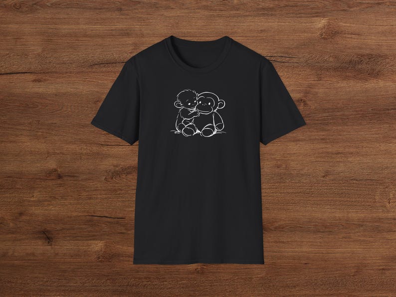 May include: Black t-shirt with a white illustration of a child embracing a monkey. The design is a simple, cartoon-style drawing of the two figures. The t-shirt has a crew neck and is made of a soft fabric.