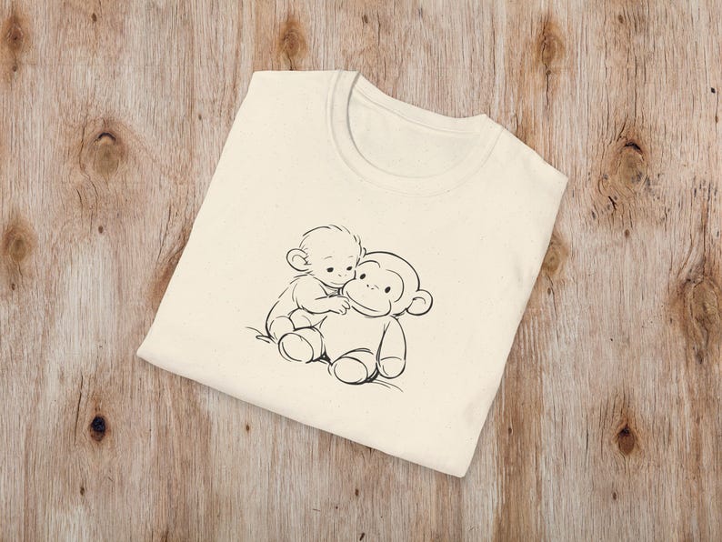 May include: Cream-coloured t-shirt with a black and white illustration of two cartoon monkeys. One monkey is sitting on top of the other. The t-shirt is made of a soft material and has a crew neck.