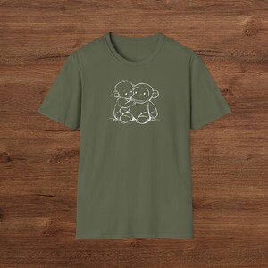 May include: Olive green t-shirt with a white outline illustration of a child embracing a monkey. The design is on the front of the crew neck, short-sleeved shirt. The shirt is made of a soft fabric.