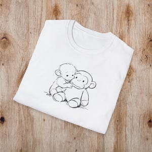 May include: White crew neck t-shirt with a black and white illustration of two monkeys. One monkey is sitting on top of the other. The t-shirt is made of a soft material and is folded on a wooden surface.