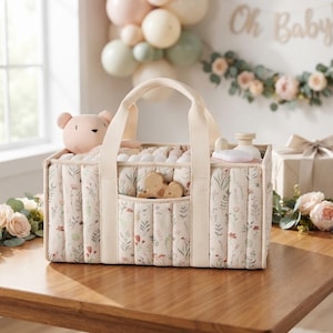 May include: A rectangular fabric storage caddy featuring a cream base with a delicate floral print in muted green, pink, and brown tones. The caddy has two sturdy cream-colored handles, vertical quilted stitching, and a small front pocket.