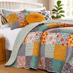 May include: A patchwork quilt and matching pillow sham featuring a repeating grid of floral and geometric patterns in shades of mustard yellow, teal, coral, and grey. A round, textured mustard yellow decorative pillow sits on the bed.