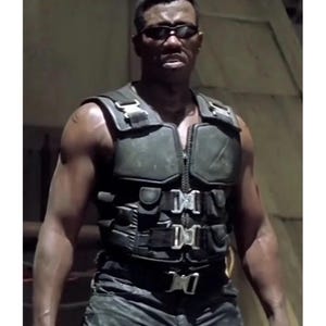 May include: A person wearing a tactical vest with multiple buckles and a zipper. The vest is dark green and has a rugged appearance. The person is also wearing sunglasses.