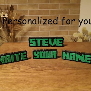 Può includere: Targhette con nome nere e verdi in stile blocco con il testo "STEVE", "WRITE YOUR NAME" e "Personalized for you". Le targhette sono su una superficie di legno.