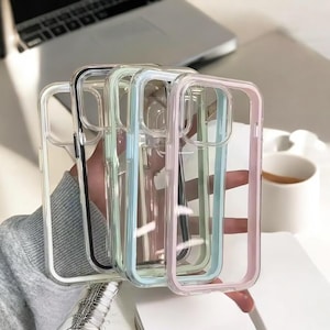 Puede incluir: Una colección de fundas transparentes para teléfonos con bordes de colores en negro, verde, azul y rosa. Las fundas están hechas de plástico transparente y están diseñadas para proteger el teléfono. Las fundas se sostienen en la mano de una persona.
