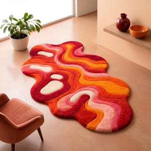 May include: An irregular, organic-shaped area rug featuring a layered, wavy pattern in shades of deep red, bright orange, soft pink, and cream. The rug has a plush, textured surface with flowing, curved lines that create a dynamic, multi-coloured effect.