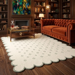May include: A rectangular area rug with a scalloped edge, featuring a cream-colored base with a repeating pattern of small, light green square outlines. The rug is positioned on a dark wood floor, showcasing its textured surface and distinct border.