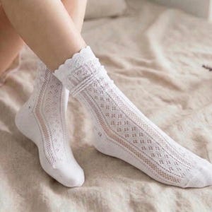 May include: White lace socks with a delicate openwork design. The socks feature a scalloped trim at the top and are knee-high. The socks are made of a soft, breathable material, perfect for adding a touch of elegance to any outfit.
