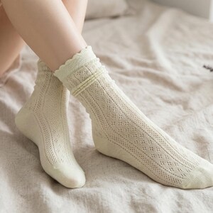 May include: A pair of cream-colored socks with a delicate openwork design. The socks have a scalloped edge and are knee-high. The socks are made of a soft, breathable material, perfect for everyday wear.
