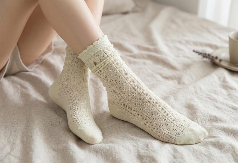 May include: A pair of cream-colored socks with a delicate openwork design. The socks have a scalloped edge and are knee-high. The socks are made of a soft, breathable material, perfect for everyday wear.