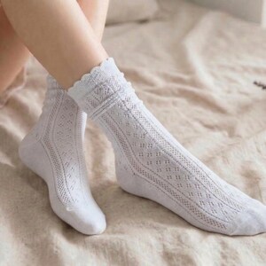 May include: A pair of white, knee-high socks with a delicate, openwork design. The socks feature a scalloped edge at the top and a diamond pattern down the length. The socks are made of a soft, breathable material.