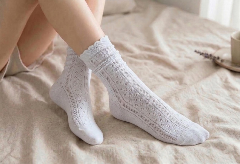 May include: A pair of white, knee-high socks with a delicate, openwork design. The socks feature a scalloped edge at the top and a diamond pattern down the length. The socks are made of a soft, breathable material.