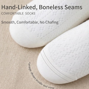 May include: Close-up of two white socks with a delicate, openwork pattern. The text "Hand-Linked, Boneless Seams" and "COMFORTABLE SOCKS" is visible. The image also includes the text "Smooth, Comfortable, No Chafing" and "*Image shows inside-out view".