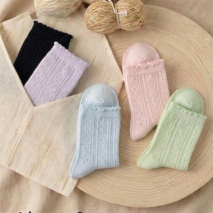 May include: Assortment of colorful socks in black, lavender, light blue, pink, and green, with a delicate openwork design. The socks are displayed with yarn balls and text that reads "Linen &bull; Cotton".