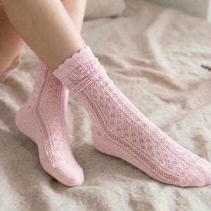 May include: A pair of light pink knee-high socks with a delicate openwork design. The socks feature a scalloped edge at the top and a diamond pattern down the leg. The socks are made of a soft, lightweight material.