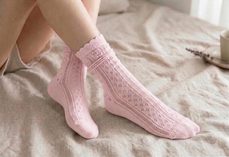 May include: A pair of light pink knee-high socks with a delicate openwork design. The socks feature a scalloped edge at the top and a diamond pattern down the leg. The socks are made of a soft, lightweight material.