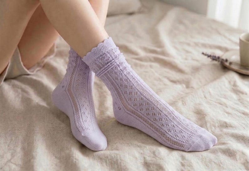 May include: A pair of lavender socks with a delicate openwork design. The socks feature a scalloped edge at the top and a diamond pattern along the leg. The socks are made of a soft, lightweight material.