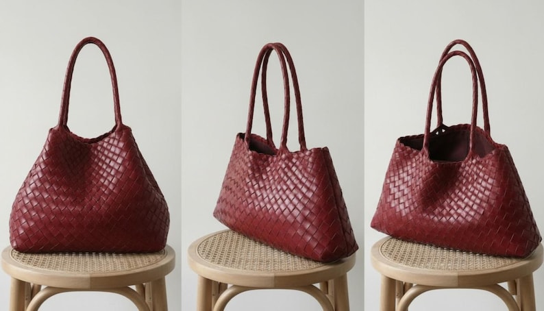 May include: A set of three burgundy-colored tote bags. Each bag features a woven design and two handles. The bags are displayed on small, round wooden stools with woven seats. The background is a plain, light-colored wall.