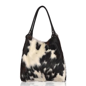 Puede incluir: Un bolso de hombro de piel de vaca en blanco y negro con un asa de cuero marr&oacute;n oscuro. El bolso tiene un aspecto suave y texturizado y un interior espacioso. El bolso est&aacute; dise&ntilde;ado con un estilo cl&aacute;sico y casual.