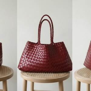 May include: A burgundy tote bag with a woven design. The bag has two long handles and is displayed on a small, round stool. The bag's texture and color are prominent, suggesting a focus on craftsmanship and style. The bag is a fashion accessory.