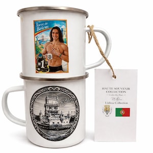 May include: Two white enamel mugs. One mug features a colourful image of a man holding a mug with the text "Torre de Belém" and "#1". The other mug has a black and white illustration of a tower. A tag is attached.