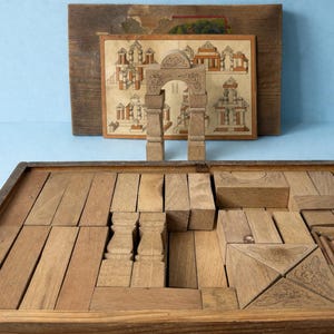 Peut inclure: Un jeu de blocs de construction architecturaux en bois vintage avec une variété de formes et de tailles, comprenant des arches, des colonnes et des blocs rectangulaires. L'ensemble est logé dans une boîte en bois, et une carte décorative avec des dessins architecturaux est incluse.