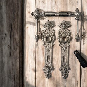 Peut inclure: Ensemble de quincaillerie de porte antique orné, comprenant une poignée, deux cache-trous de serrure et des composants associés. Les pièces métalliques présentent un design vintage détaillé avec une finition argentée, montées sur une porte en bois clair.