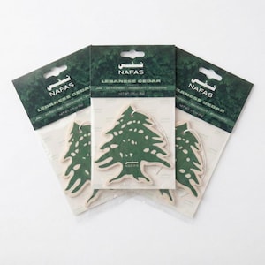 May include: Three Nafas brand air fresheners shaped like Lebanese cedar trees. Each green tree-shaped air freshener is packaged in a clear plastic sleeve with a dark green header card featuring the text Nafas and Lebanese Cedar, net weight 0.11 oz.