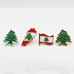 May include: A set of four metal enamel pins featuring symbols of Lebanon. Two pins are shaped like green cedar trees, one is the outline of the country of Lebanon with the national flag colours, and one is a rectangular waving Lebanese flag.
