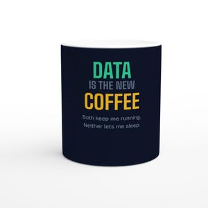 Könnte beinhalten: Ein dunkelblauer Keramikbecher mit dem Text "DATA IS THE NEW COFFEE" in Grün und Gelb, gefolgt von dem kleineren weißen Text "Both keep me running. Neither lets me sleep." Der Becher hat eine zylindrische Form und eine glatte Oberfläche.