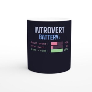 Könnte beinhalten: Ein dunkelblauer Keramikbecher mit dem Text "INTROVERT BATTERY:" in Hellblau und Weiß. Darunter zeigen drei Fortschrittsbalken "Social event: 42%" in Pink, "After event: 3%" in Pink und "Alone + code: 100%" in Hellgrün an.