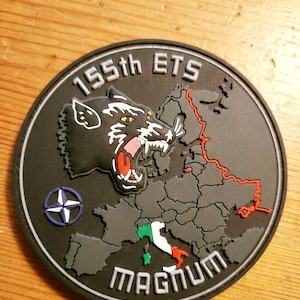 Könnte beinhalten: Ein runder, schwarzer Aufnäher mit dem Text "155th ETS" und "MAGNUM". Der Aufnäher zeigt einen knurrenden Panther, eine Europakarte und ein NATO-Symbol. Die Karte hebt Italien mit grünen, weißen und roten Farben hervor.