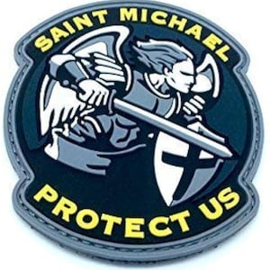 May include: A circular patch depicting Saint Michael with a sword and shield, bearing a cross. The words "SAINT MICHAEL PROTECT US" are in yellow around the edge. The design features a black background with grey and white details.
