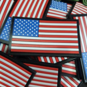 May include: Rectangular patches featuring the American flag design. The patches have a blue field with white stars in the upper left corner and red and white stripes. The patches are framed in black.