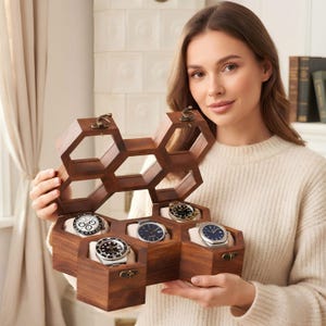 May include: A hexagonal wooden watch box with a hinged lid, featuring a honeycomb-inspired design. The interior contains four individual compartments, each holding a wristwatch on a soft cushion. The box is crafted from dark brown wood.