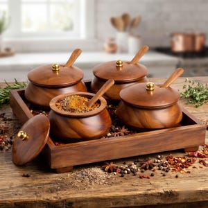 May include: A set of three round wooden spice bowls with matching lids and spoons, arranged on a rectangular wooden tray. Each bowl features a smooth finish and a small gold-toned knob on the lid. One bowl is open, revealing colorful spices.