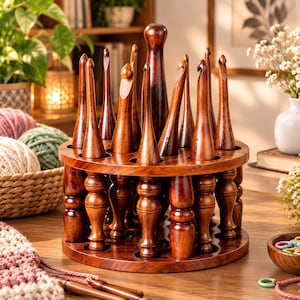 Puede incluir: Un soporte giratorio de madera marrón oscuro que contiene varios ganchos de ganchillo de madera pulida de diferentes tamaños. El soporte circular cuenta con un mango central y patas torneadas decorativas, con cada gancho insertado en una ranura.