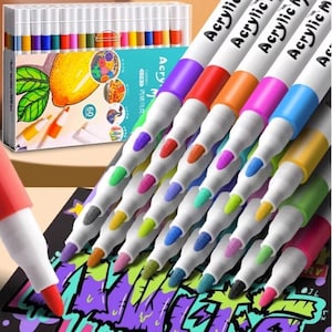 Op de afbeelding: Een set van 60 acrylverfmarkers met witte behuizingen en gekleurde doppen, gerangschikt in een diagonale stapel. De markers hebben fijne punten in diverse kleuren, waaronder paars, rood, oranje, roze, blauw, geel en groen, op een zwart oppervlak.