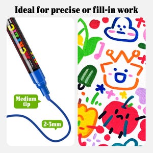 Puede incluir: Un marcador de pintura acrílica azul con cuerpo negro y texto blanco, que presenta una punta mediana con un ancho de trazo de 2-3 mm. El marcador dibuja una línea azul junto a una superficie blanca con ilustraciones de dibujos coloridos.