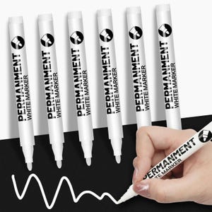 Op de afbeelding: Een set van zes witte permanente markers met zwarte tekst die PERMANENT WHITE MARKER leest. Elke marker heeft een cilindrische behuizing en een witte dop. Eén marker wordt gebruikt om een witte golvende lijn op een zwart oppervlak te tekenen.