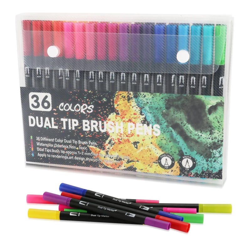 Op de afbeelding: Een set van 36 dual-tip penseelstiften in een doorzichtige plastic etui. De verpakking bevat de tekst 36 COLORS DUAL TIP BRUSH PENS en toont een aquarel-stijl afbeelding. Verschillende stiften met gekleurde doppen liggen voor de etui.