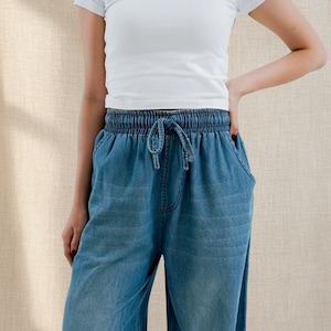Könnte beinhalten: Hellblaue Jeanshose mit elastischem Bund und Kordelzug. Die Hose hat zwei Vordertaschen und eine lockere Passform. Das Model trägt ein weißes T-Shirt.