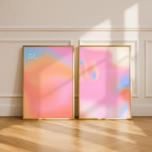 May include: Two rectangular wall art prints in thin gold frames. The left print features a gradient of pink, orange, and blue with the text "what if it all works out" in white. The right print displays a soft, abstract gradient of pink and blue.