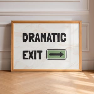 Op de afbeelding: Een ingelijste kunstprint met de woorden "DRAMATIC EXIT" in zwarte letters. Daaronder staat een groen bord met een witte pijl naar rechts. De lijst is lichtbruin en de achtergrond is een getextureerde gebroken witte kleur.