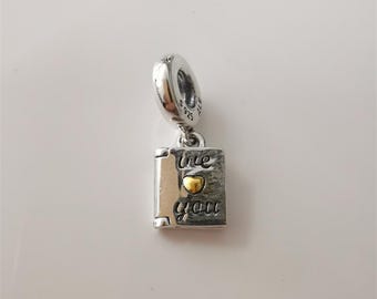 May include: Silver charm with a small book design. The book has the words "I love you" engraved on it, with a gold heart in the center. The charm is attached to a silver loop.