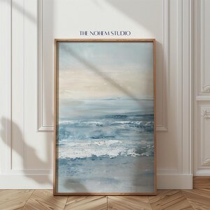 Puede incluir: Impresión artística abstracta de un paisaje oceánico en un marco de madera. La obra de arte presenta tonos de azul, gris y blanco, que representan olas y una línea de horizonte. El texto "THE NOHEM STUDIO" está en la parte superior. El arte enmarcado se exhibe contra una pared blanca.