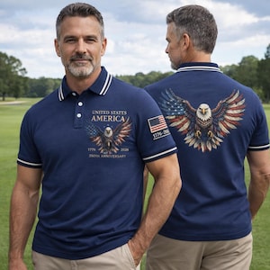 May include: Navy blue polo shirt with white trim and a patriotic eagle design. The shirt features the text "UNITED STATES AMERICA" and "1776-2026 250TH ANNIVERSARY" with an American flag graphic. The back of the shirt also displays an eagle with outstretched wings.