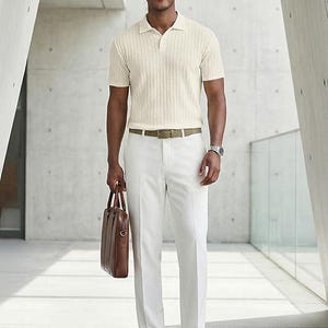 May include: A short-sleeved cream-colored polo shirt with a textured knit pattern, paired with crisp white trousers, a tan leather belt, brown leather loafers, and a brown leather briefcase. The outfit is accessorized with round sunglasses and a watch.
