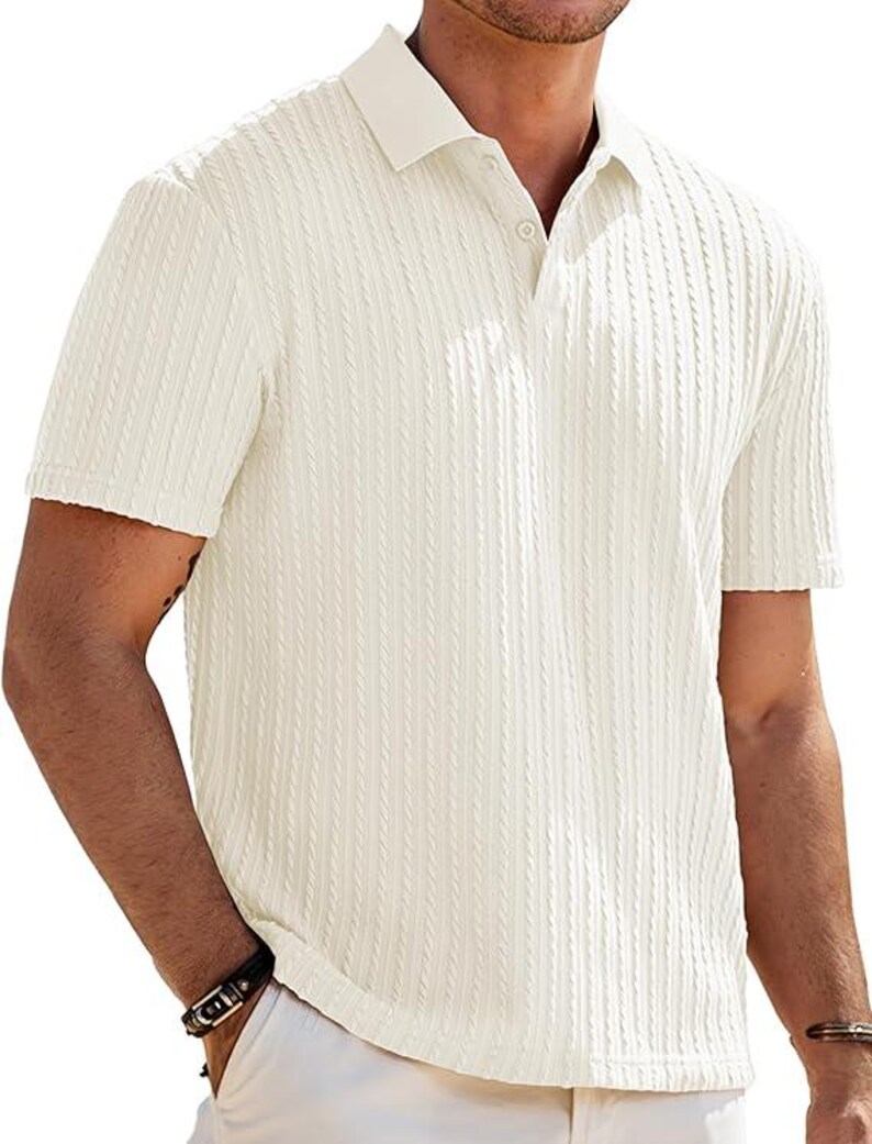 May include: A short-sleeved polo shirt in an off-white color featuring a vertical textured cable knit pattern. The shirt has a classic collar, a buttoned placket with visible buttons, and a straight hemline, providing a clean and structured appearance.