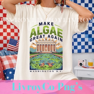Könnte beinhalten: Ein cremefarbenes T-Shirt mit einem Grafikdruck des Lincoln Memorials, einem mit grünen Algen bedeckten Teich und zwei Enten. Der Text MAKE ALGAE GREAT AGAIN und WASHINGTON D.C. ist in dunkelblauer und grüner Schrift auf der Vorderseite.